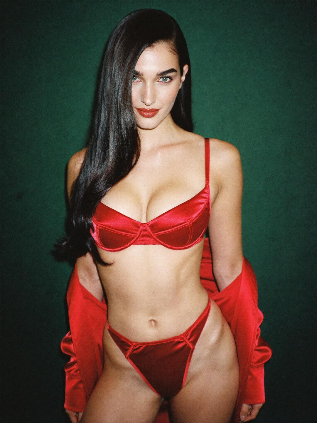 Ava in red satin lingerie and a red satin robe against a dark green wall