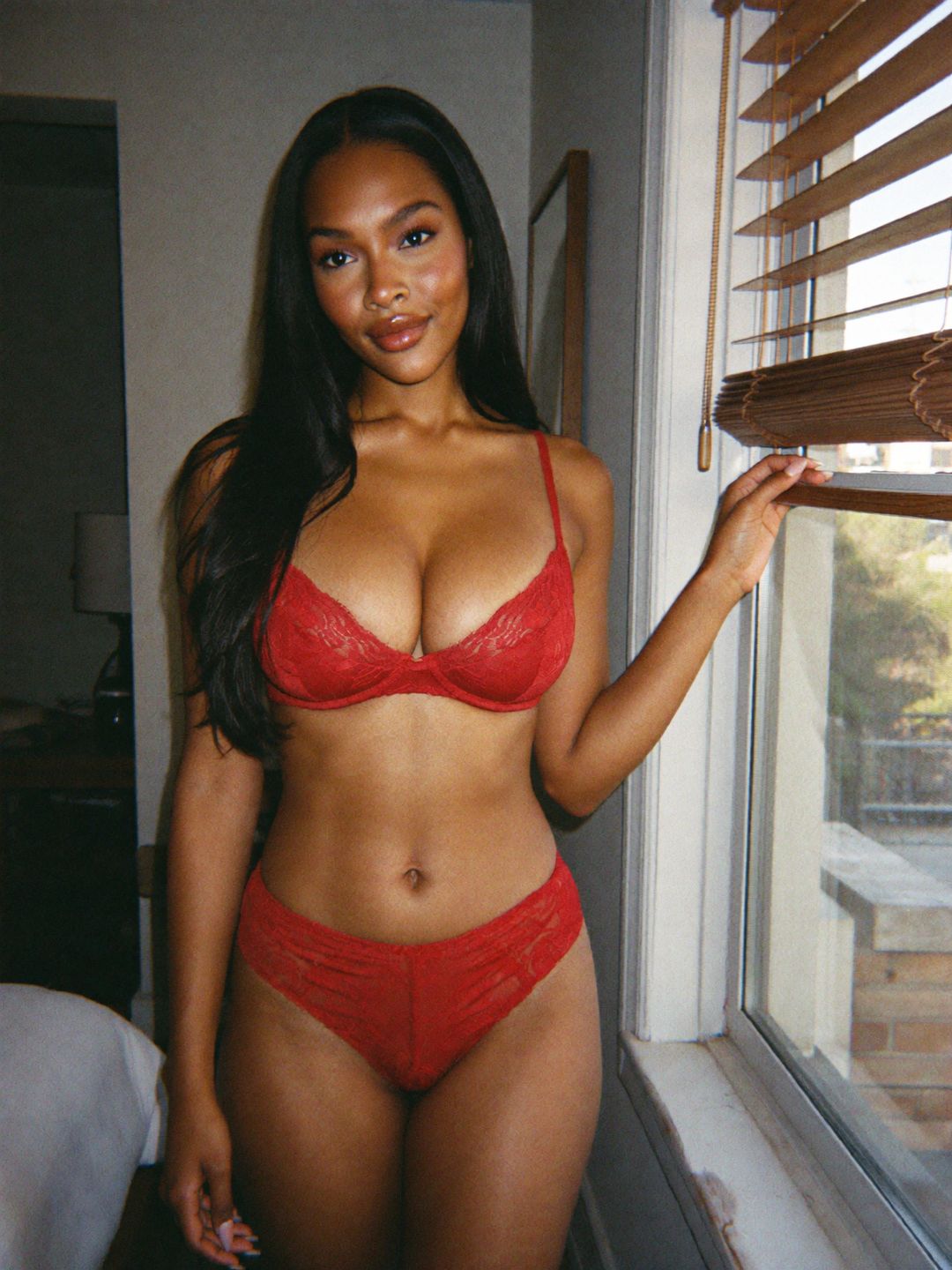 Kira in red lace lingerie by the window of a sunlit Los Angeles bedroom